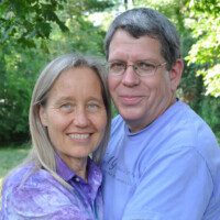 Smiling couple posing outdoors with a green background.